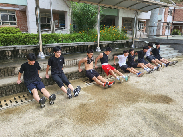 ▲ 학남중 복싱부 선수들이 학교 운동장에서 팔 근력 운동에 매진하고 있다.